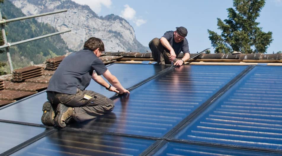 Due montatori fissano i collettori di un impianto solare termico su un tetto inclinato esposto al sole.
