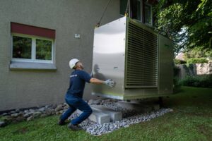 Une pompe à chaleur fixée à une grue est mise en place par un ouvrier.