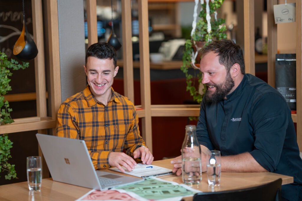 zwei Männer sitzen am Tisch und betrachten einen Laptop-Bildschirm